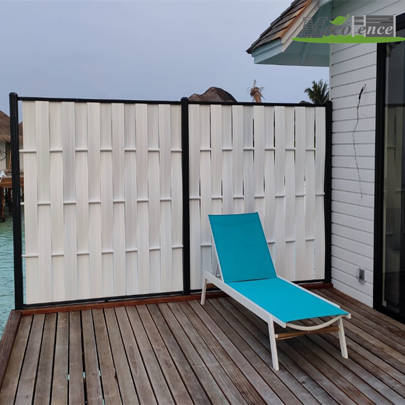 A privacy screen made of white woven composite fence panels with black framing installed on a wooden resort deck set on the sea.