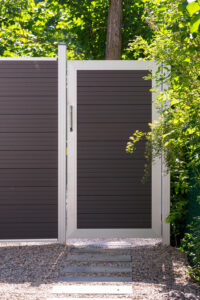 Long brown Mecofence WPC composite horizontal slatted perimeter fence gate installed on a slope next to a road, providing durable, scalable boundary solutions for commercial and residential constructors globally.
