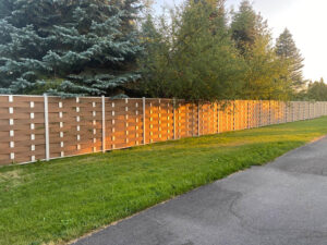 Long light brown Mecofence woven WPC composite fence enclosing a wooded property in Lyon, France, offering a distinctive, wind-resistant boundary solution for commercial constructors.