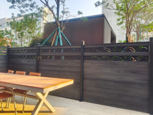 tall dark grey WPC composite privacy fence enclosing a large suburban backyard with extensive lawns and mature deciduous trees in the background, typical of UK properties.