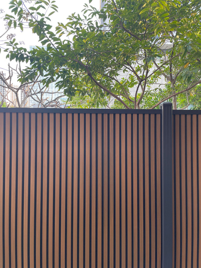 Vertical fluted composite fence with contrasting wood-tone faces and dark grooves.
