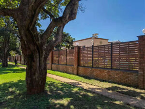 Brown Mecofence WPC slatted fence on a brick wall, providing durable, ventilated boundaries for commercial constructors in warm climates.