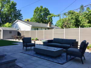 Light brown WPC composite privacy fence with light metal posts enclosing a modern backyard patio and seating area.