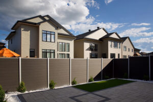 Corner view of a solid brown WPC composite privacy fence with modern metal posts separating a suburban backyard.Suburban housing developments across North America and Europe