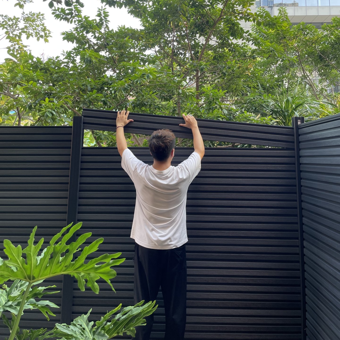 Close-up of hands installing low-maintenance composite privacy fence with deep woodgrain texture