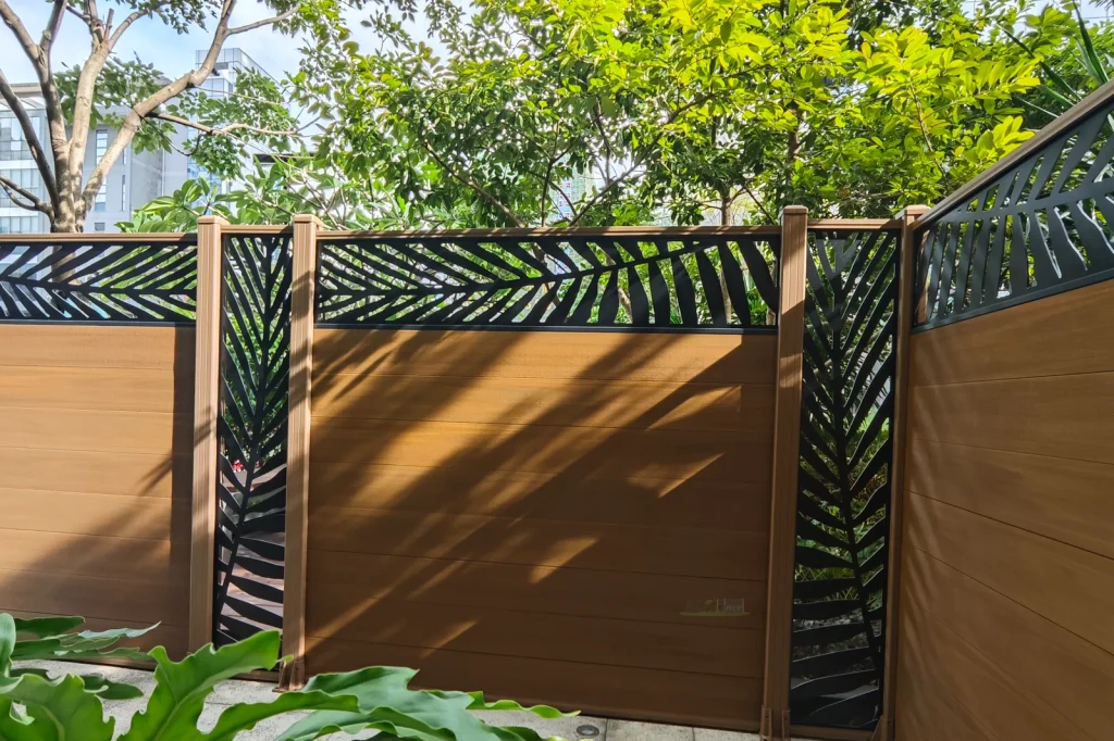 Woodgrain composite fence with black leaf-pattern aluminum screens across the top and between panels