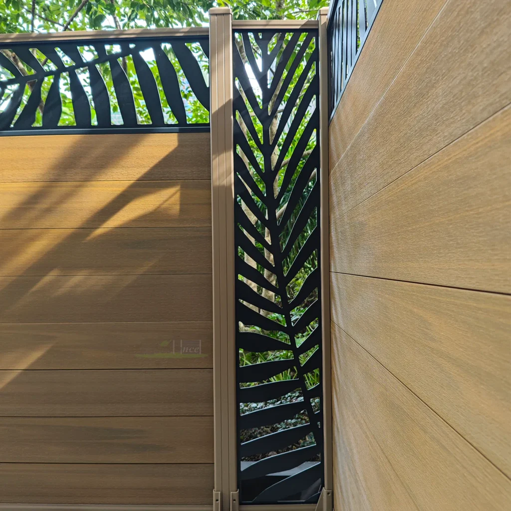 Close-up of a black leaf-pattern aluminum screen between woodgrain composite fence panels