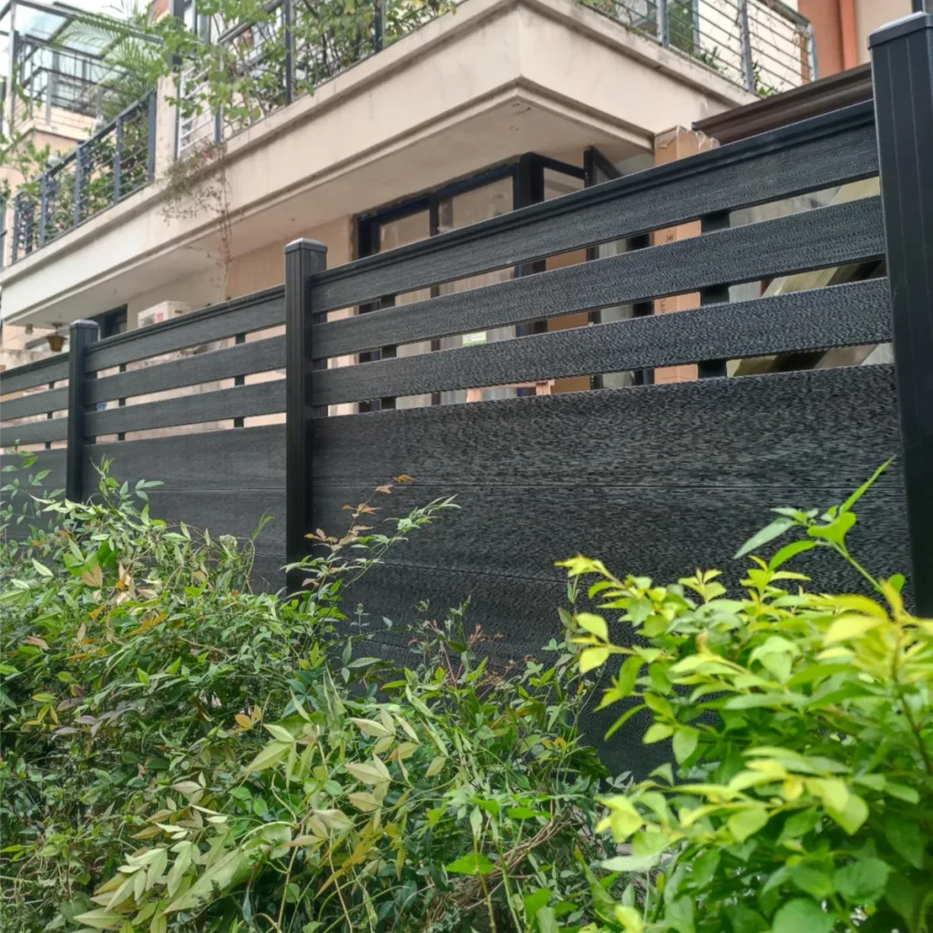 Installer positioning a dark grey Mid-Trellis fence board between structural posts