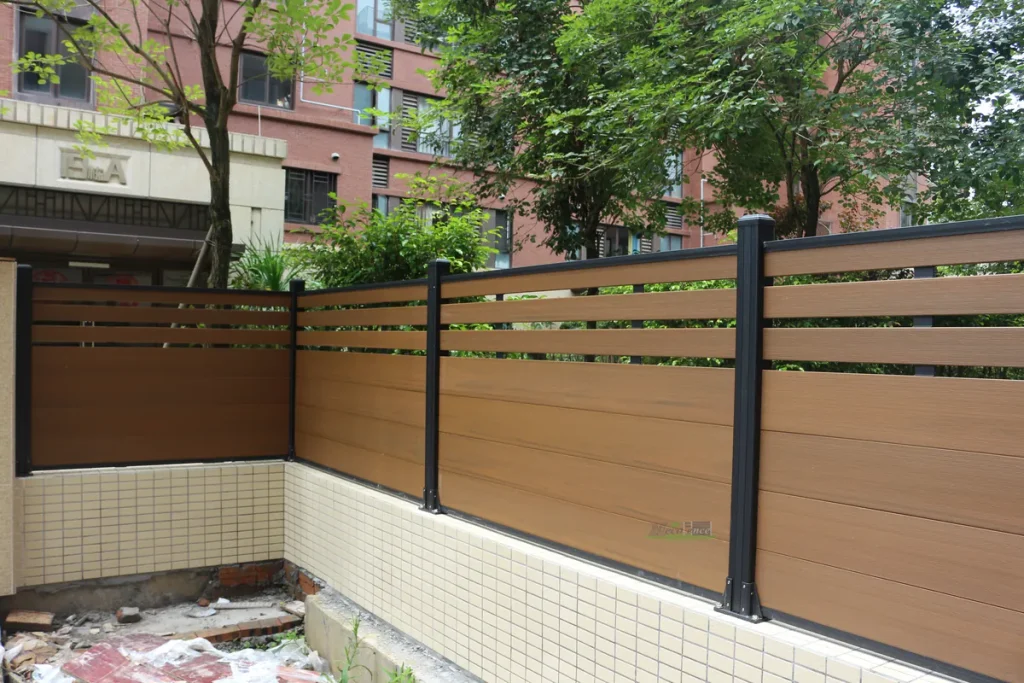 Teak Mid-Trellis Composite Fence with black aluminium posts along a corner boundary wall