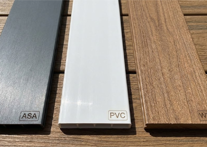 A detailed photograph of three fencing material samples—dark grey ASA with a brushed finish, smooth white PVC, and brown wood-grain WPC—laid side-by-side on a wooden surface.