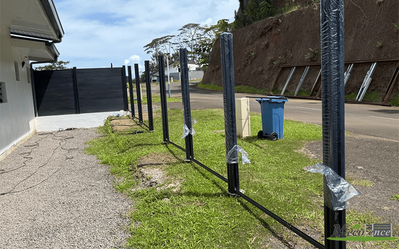 Co-extruded WPC fence posts and steel base rails being installed along a hillside in French Polynesia