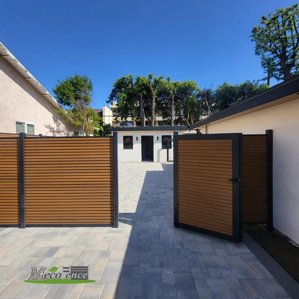 Teak fluted composite fence with a matching swing gate and black aluminum frame at a paved courtyard entrance