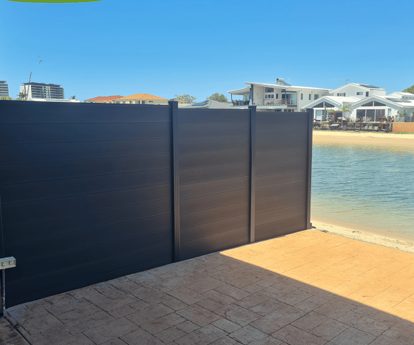MecoFence 6ft Modern black composite privacy fencing panels installed next to a coastal shore with residential houses in the background.